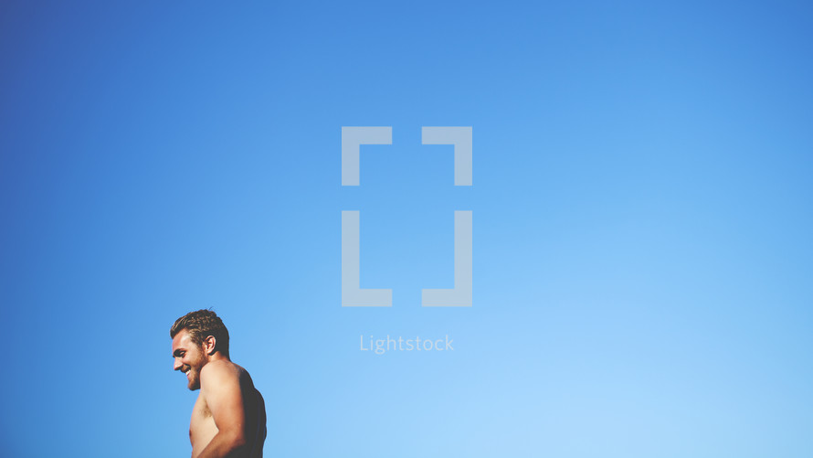 shirtless man against a blue sky backdrop 