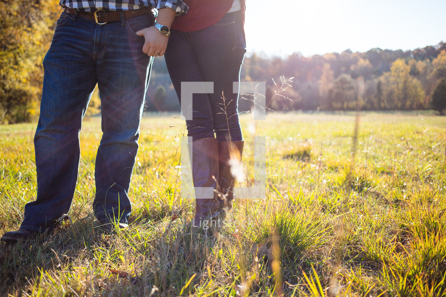 Couple holding hands as they walk through a field of grass.