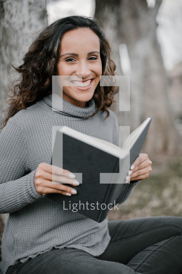 A smiling young woman reading a book 