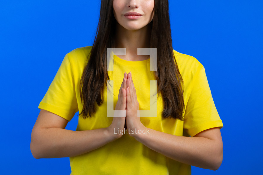 Calm woman praying with namaste, meditating. Unrecognizable lady calms down, breathes deeply on blue studio background. Yoga concept. High quality photo