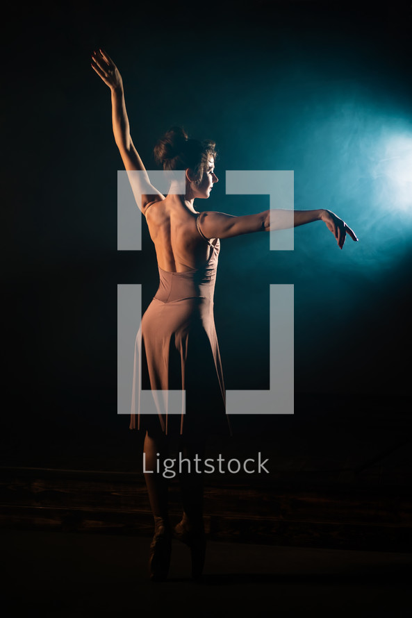 Incredible ballerina woman dancing ballet on stage in front of spotlight. Volumetric painting, smoke scene. 
