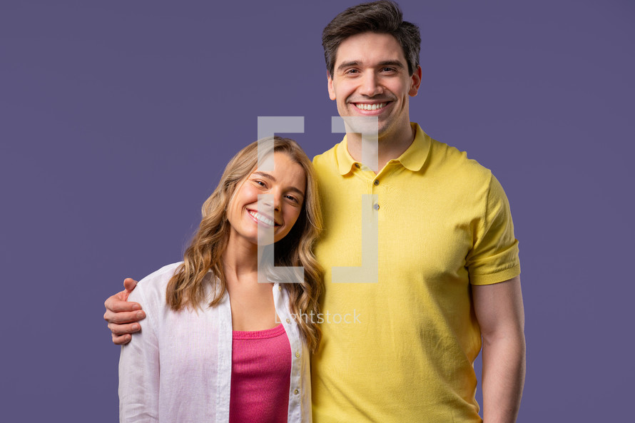 Pretty woman young adult man portrait on violet studio backdrop. Friendly couple smiling. Colorful vibrant outfit. High quality