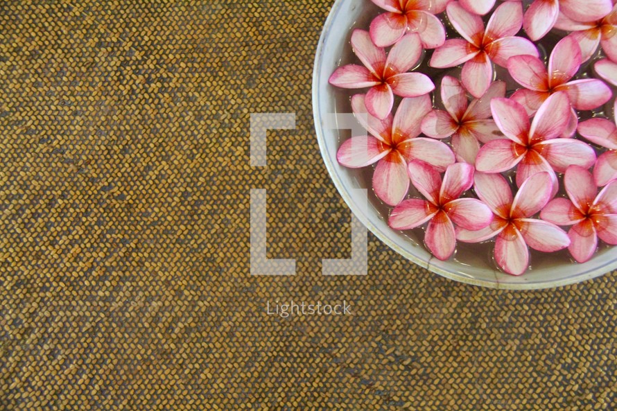 Bowl of pink tropical flowers on a woven mat