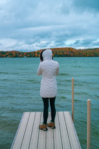 a woman in a coat standing on a dock in fall 