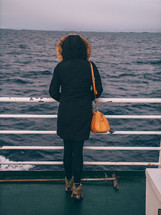 a woman looking over railing of a boat at the water 