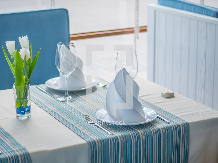 Interior design of a beautiful restaurant in a marine style. Table setting with glasses, plates, napkins and flowers