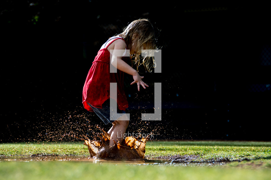 Child splashing in a mud puddle.
