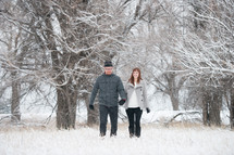 a couple walking and holding hands in the snow 
