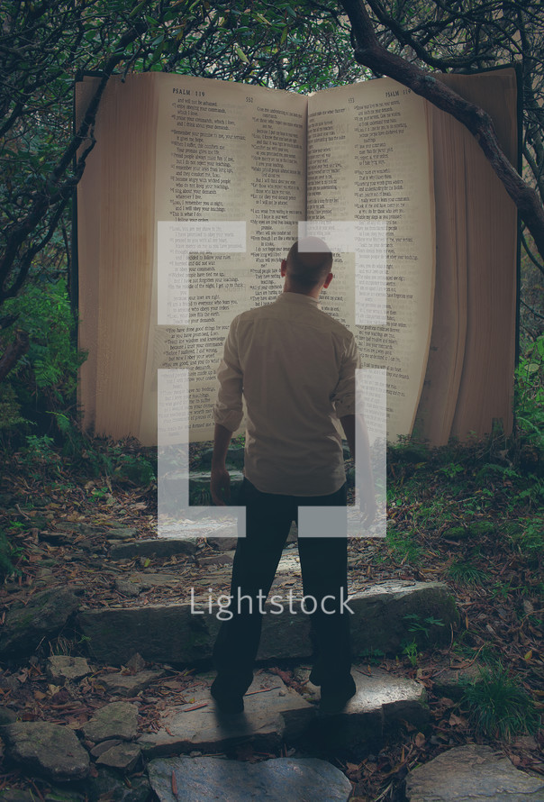 man standing in front of a giant Bible in a forest 