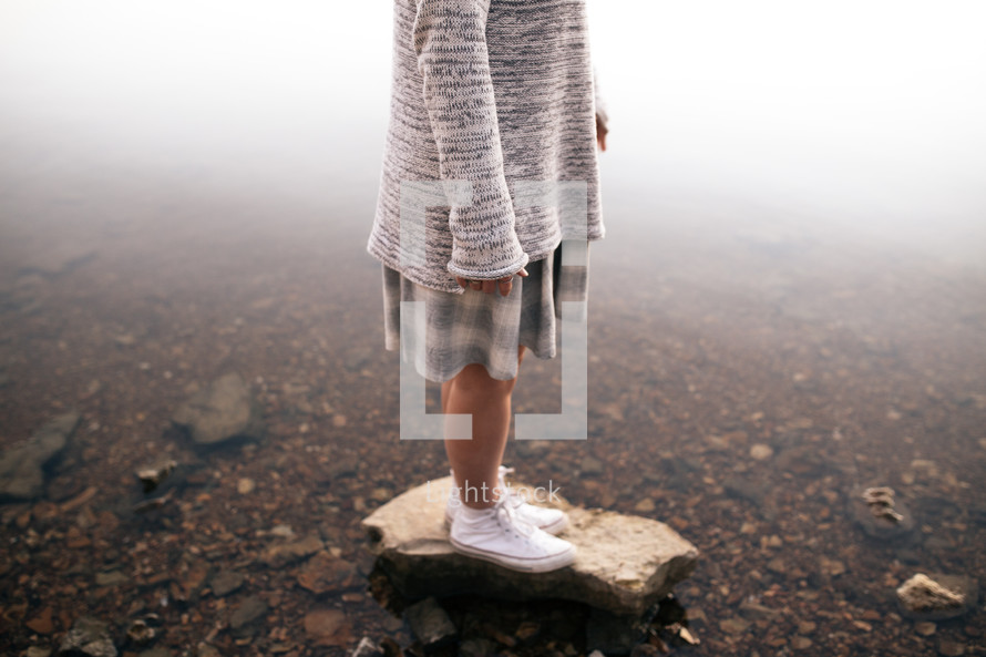 a girl standing on a stone in a pond 