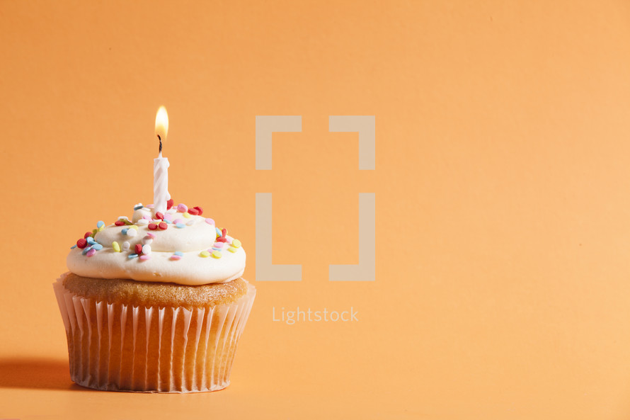 cupcake with candle against an orange background 