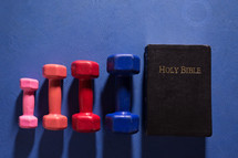 Dumbbells on a blue gym workout mat next to the Holy Scriptures