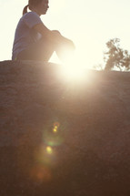woman sitting on top of a rock under sunlight