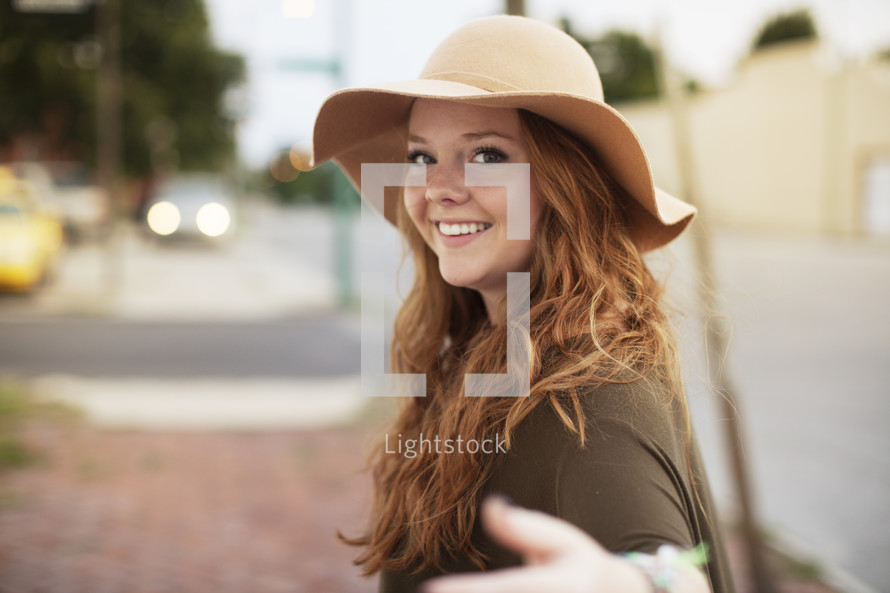 a young woman in a hat, gesturing to come this way 