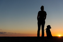 silhouette of a woman and her dog at sunset 