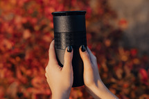 Woman hands holds black thermos cup with fresh coffee. Drinking in autumn forest. Enjoy nature, holidays on mountains. High quality