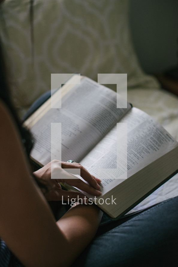 young woman reading a Bible on a bed 