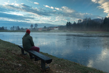 man sitting on a bench looking out at a lake 