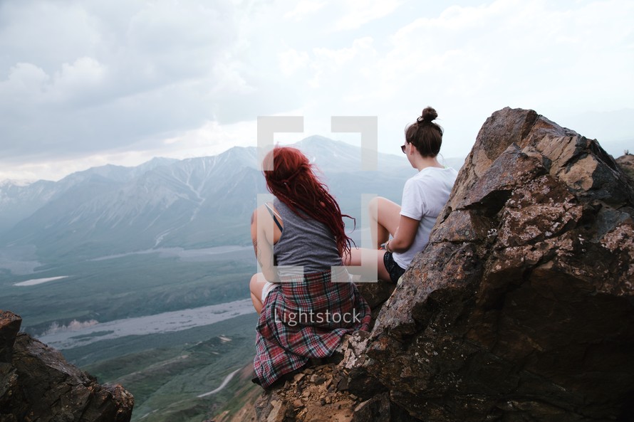 women sitting on rocks on the edge of a mountain 