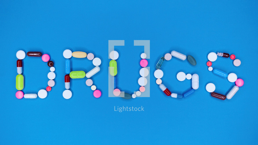 Multicolored capsules in word drugs. Blue background. Pharmacy, antidepressants, medicine concept. High quality photo