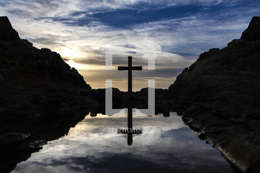 silhouette of a cross at sunset near a tide pool 