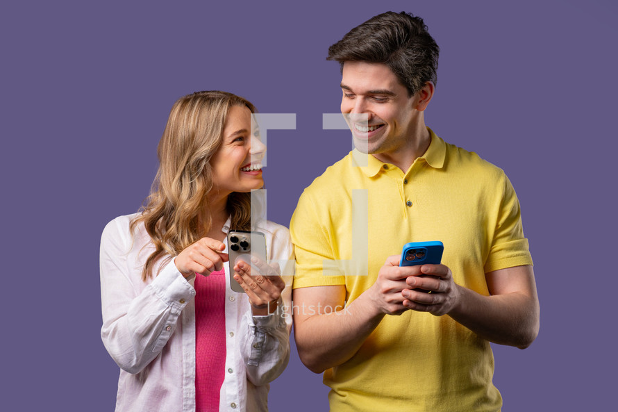 Young couple using mobile device. Woman and man watching, talking, smiling, laughing with smartphone. Social apps, networks, technology concept. Violet studio background.