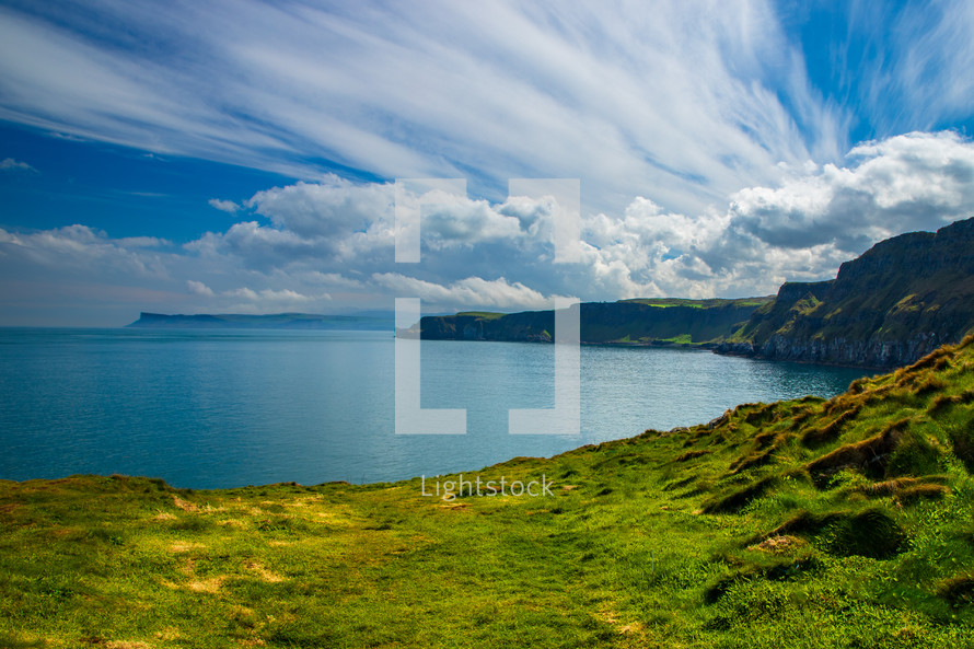 A dramatic sky over bright green field of grass and sea cliffs in Northern Ireland.
