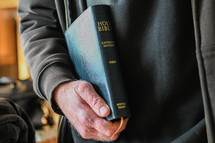 elderly man holding a Bible at his side