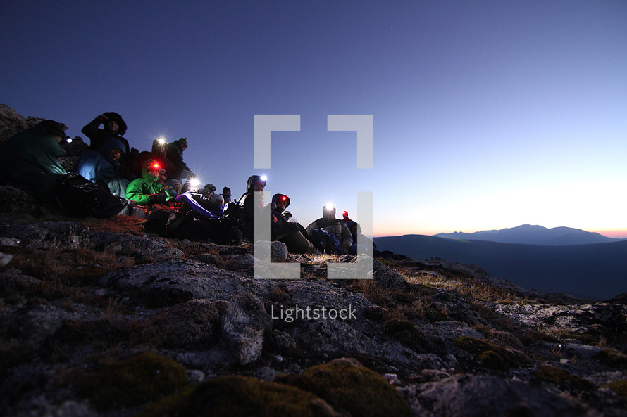 hikers with headlamps sitting on a mountainside 