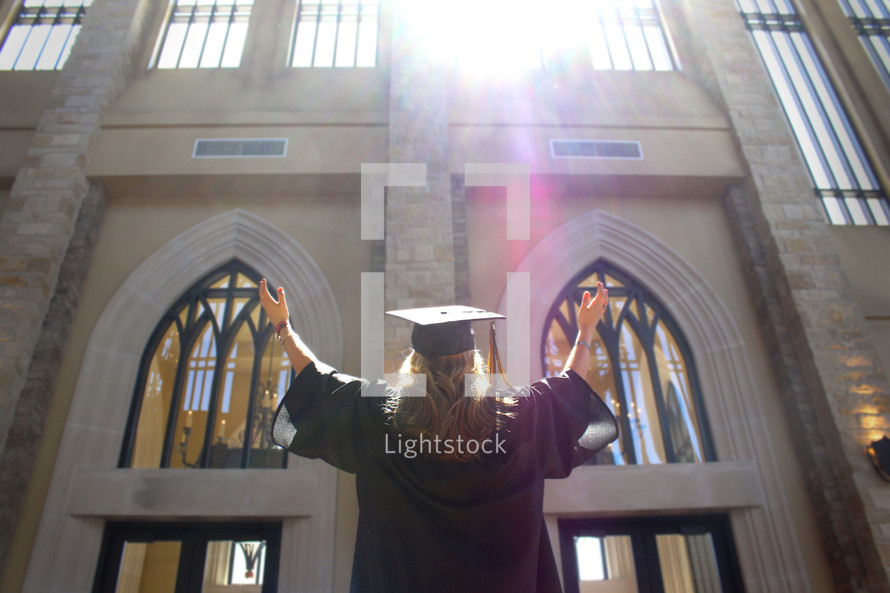 girl in cap and gown with her hands raised in worship to God