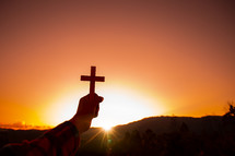 arm holding up a cross against an orange sky at sunset 