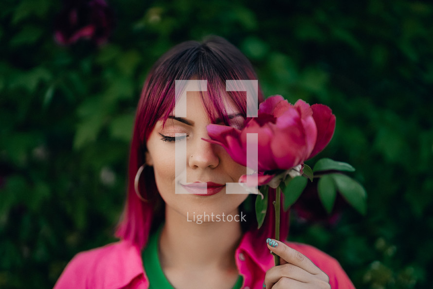 Portrait of real serene woman with vivid dyed pink fuchsia hairstyle. Peony flower, green nature backdrop. Trendy colorful hair, stylish haircut