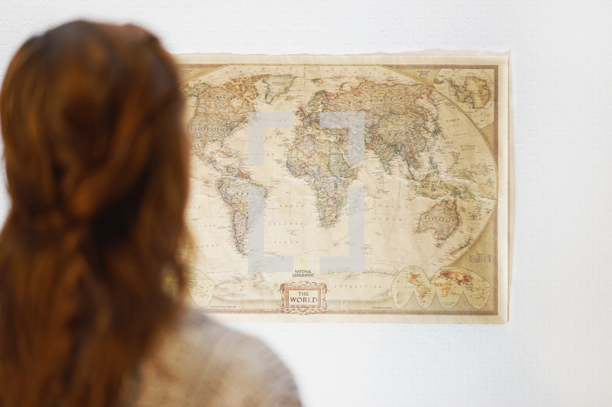 A woman looking at a world map hanging on a wall 