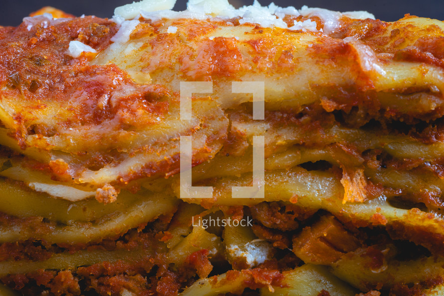 Close up view from a home made Lasagna, on a wooden table, and a dark background.
