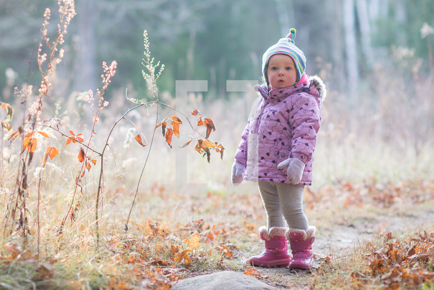 a toddler girl in a coat standing outdoors 