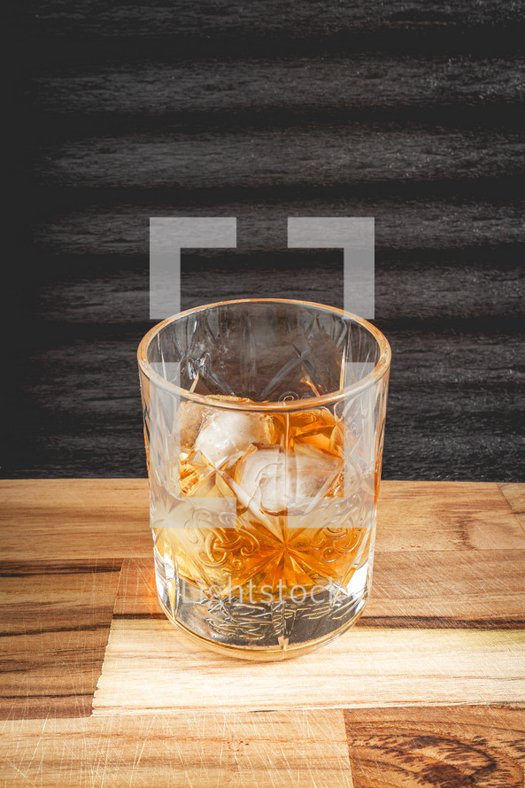 A glass of wiskey on the Rocks, on a black background, and a wooden table.