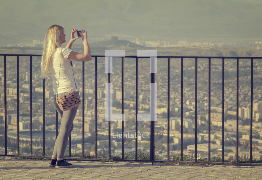 a woman taking picture of a city standing near a railing 