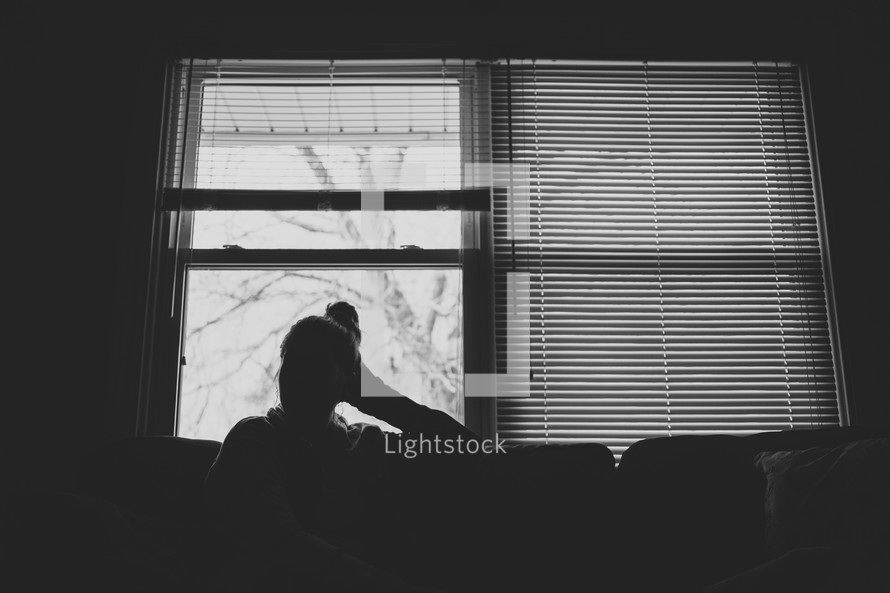 woman sitting on a couch thinking in front of a window 