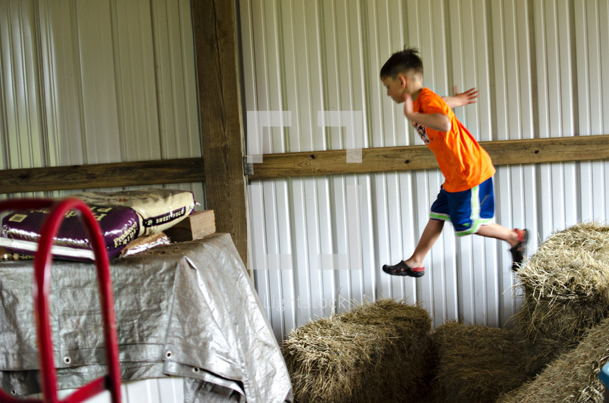 boy jumping on hay bales 