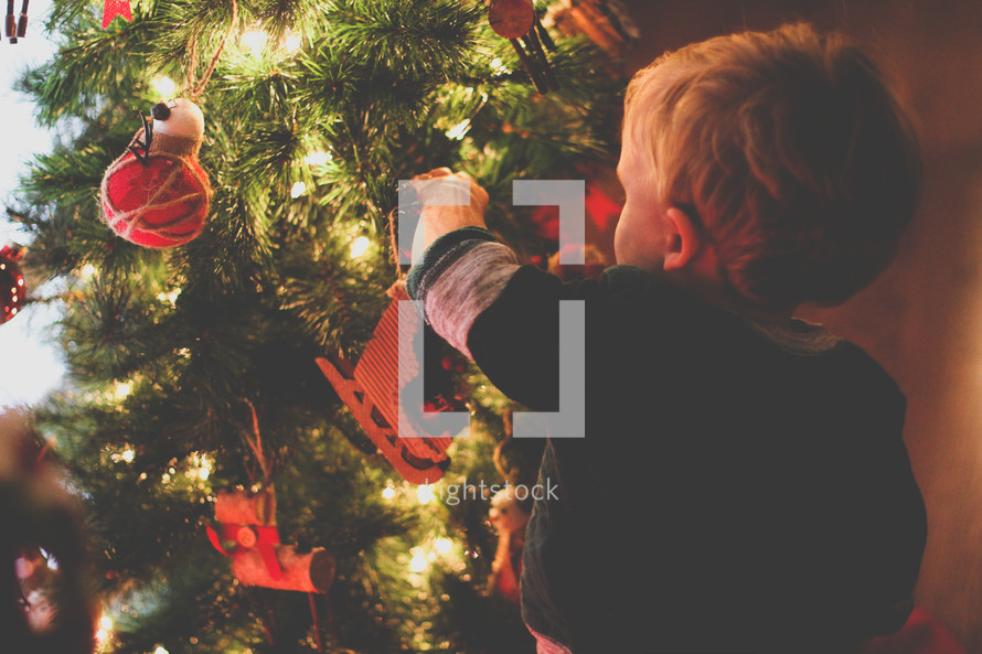 a toddler boy decorating a Christmas tree 