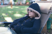 a woman in a hoodie lying in a lounge chair 