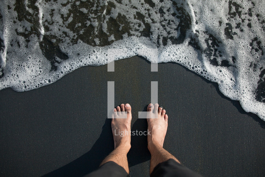 bare feet standing on a shore at the edge of the water 