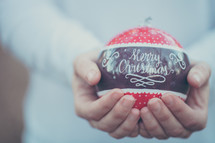 an large red ornament with the words Merry Christmas in a man's hands 