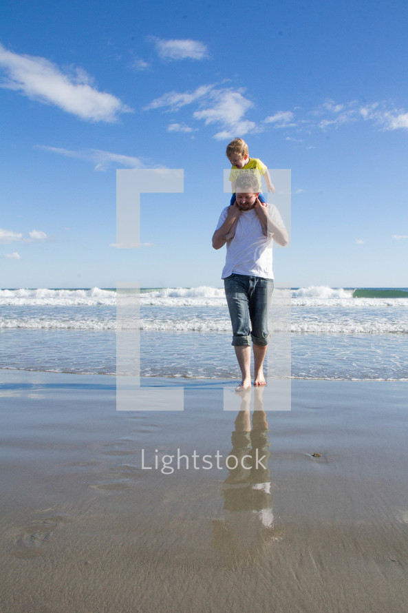 Child riding on Father's shoulders at the beach on a sunny day.