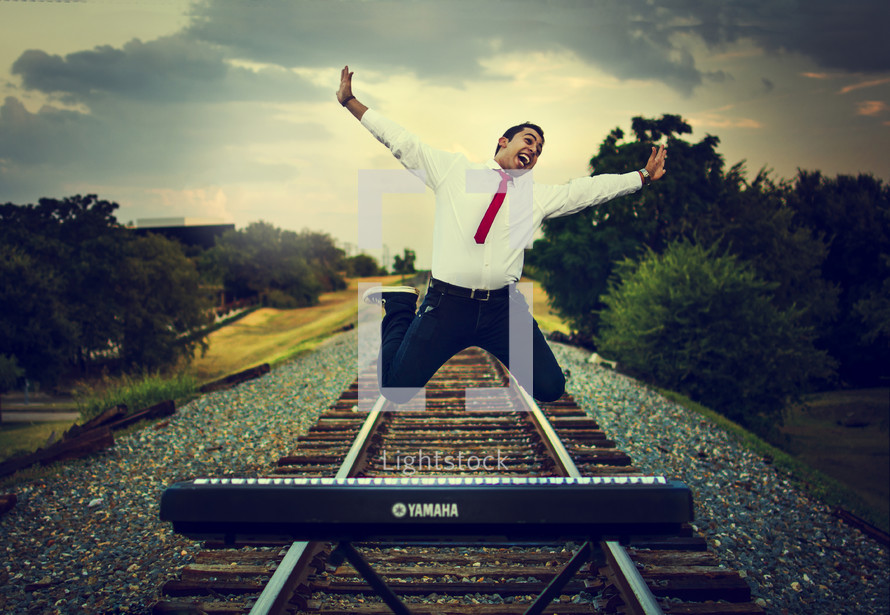 man jumping for joy on train tracks with a digital piano 