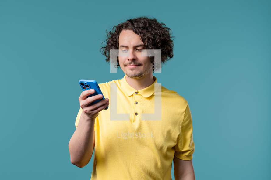 Handsome male model surfing internet on smartphone. Man with smile and joy on blue background. Tech, success, happiness, social networks concept. High quality