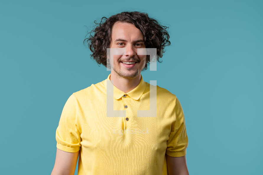 Friendly 30s white man smiling portrait. Positive curly guy in yellow polo on blue studio. High quality photo