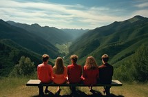 Group of friends sitting on a bench in the mountains and looking at the valley