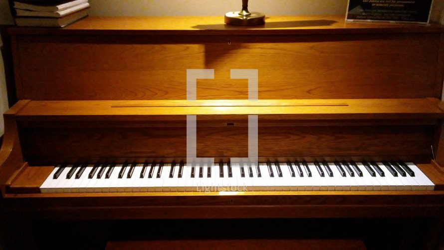 A closeup view of the piano keys and wooden body of a Church piano lit in an church sanctuary. 