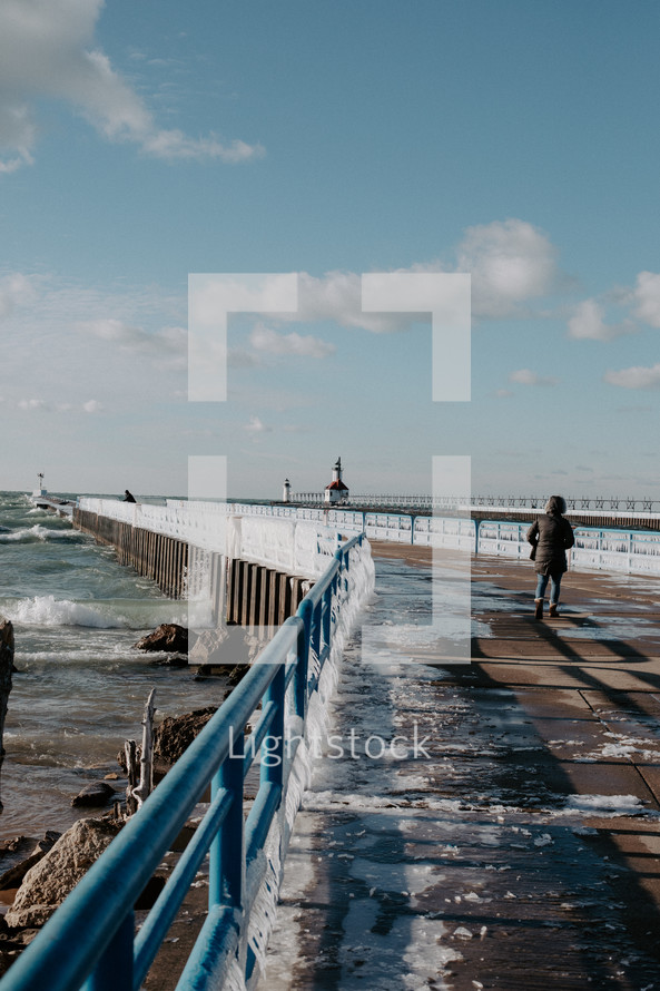 Ice covered railing on beach pier leading out to a lighthouse on Lake Michigan